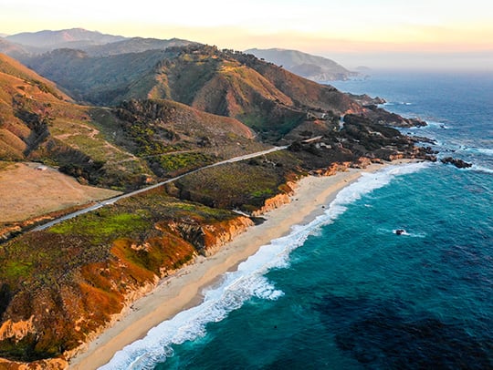 Aerial view of a coastline with a road and hills in the background