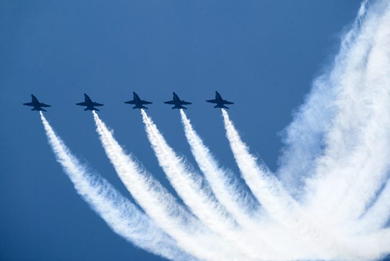 Cinq jets de combat volant en formation dans un ciel bleu.